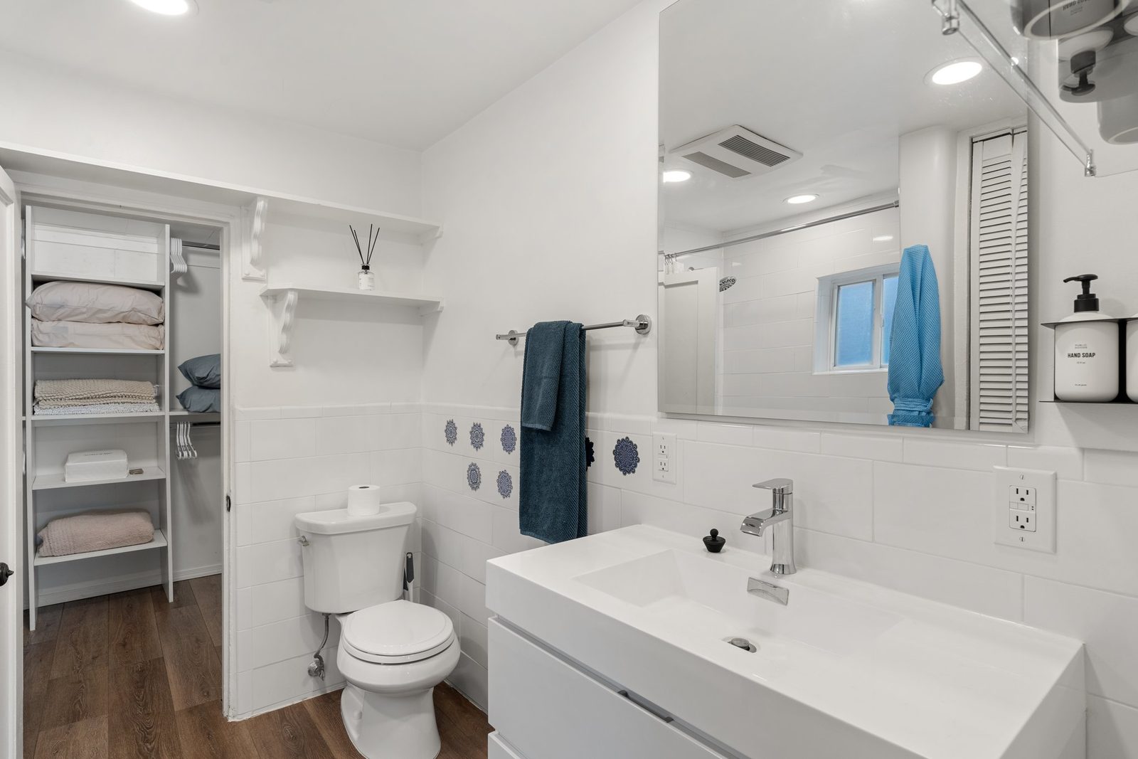 The bathroom: a wide white vanity with a mirror above it, open shelving stacked with towels.