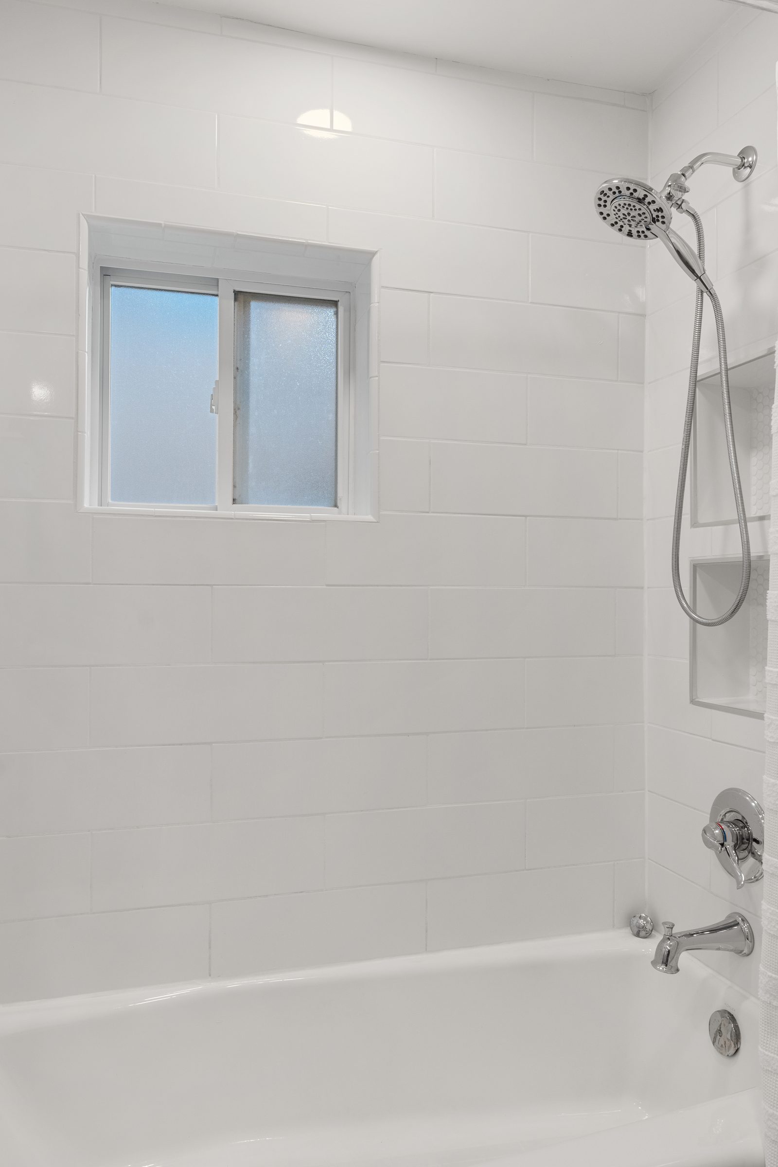 The casita bathroom now: white subway tile, a rain shower head, and the same window looking out from a fresh tub surround.