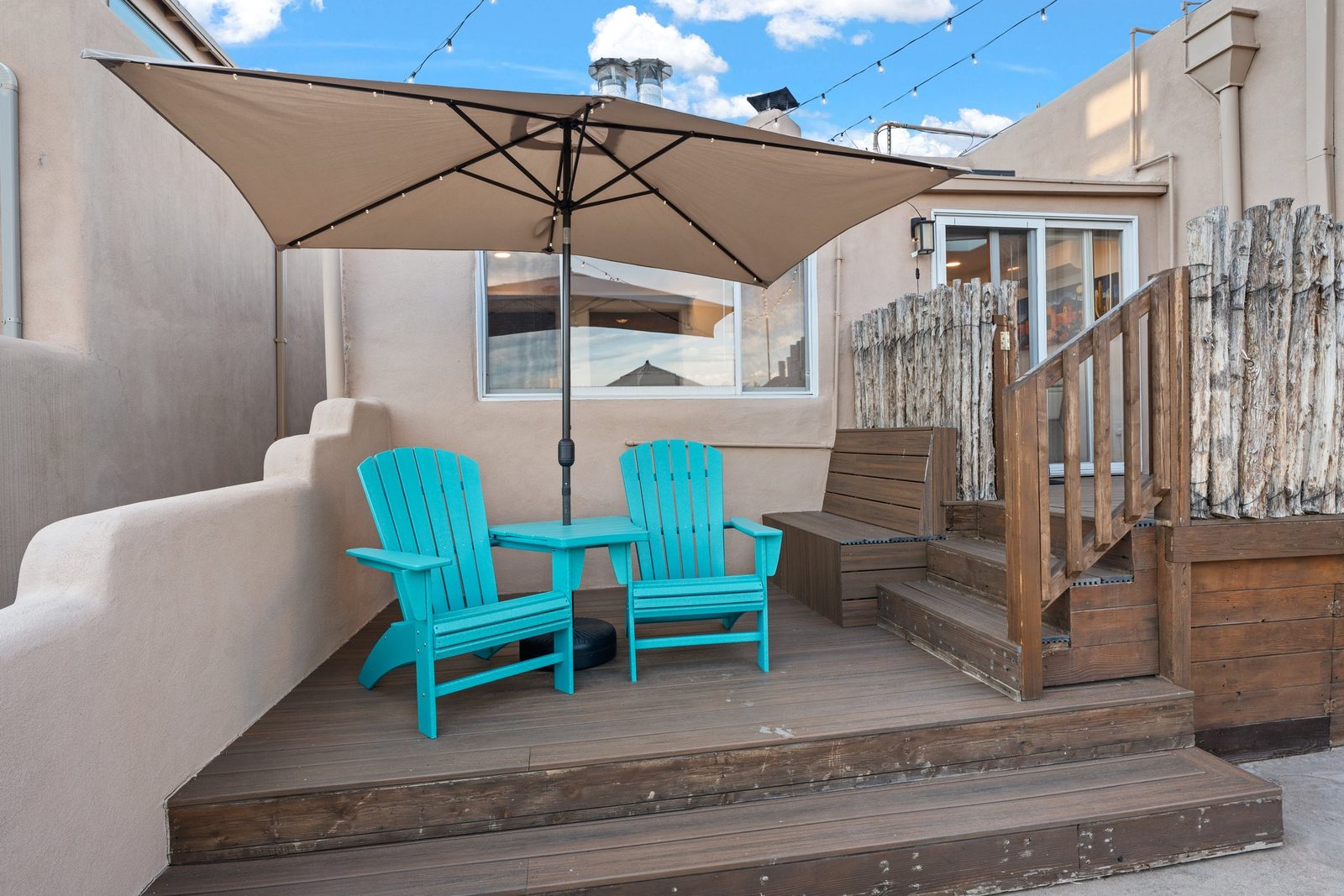 Two turquoise Adirondack chairs under an umbrella at the corner of the deck, the best of the evening light.