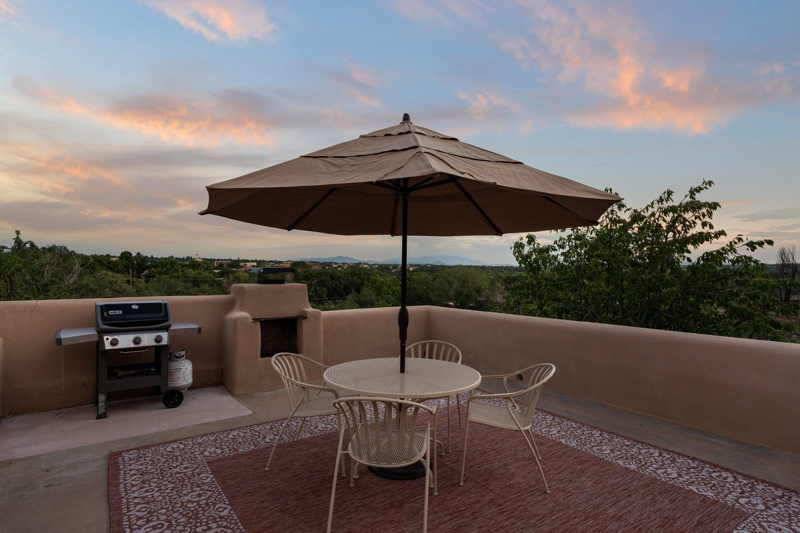 The grill and the dining table on the deck as the light goes, the city spread out beyond the fence.