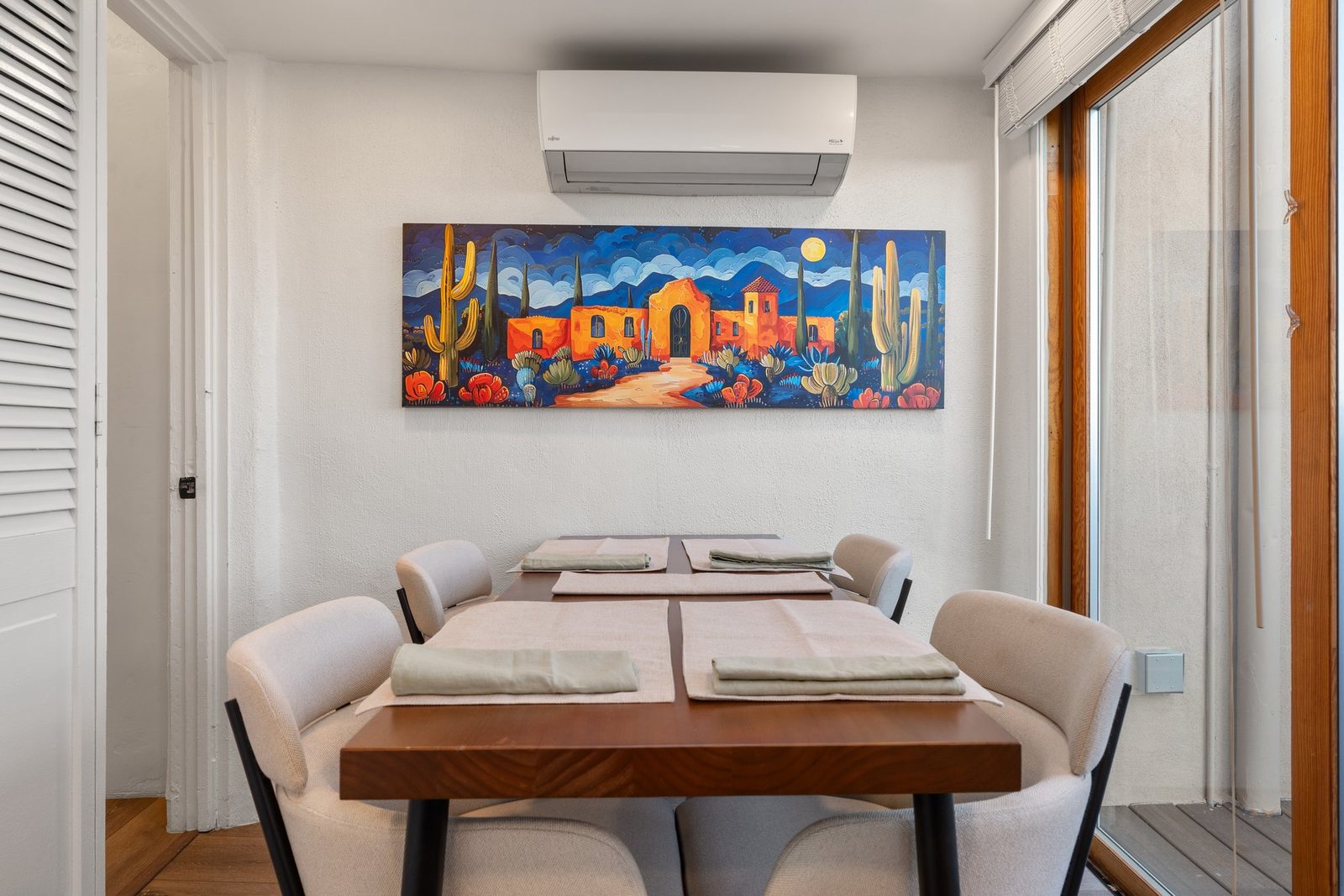 The dining table set for two under a bright painted desert mural, with the mini-split above.